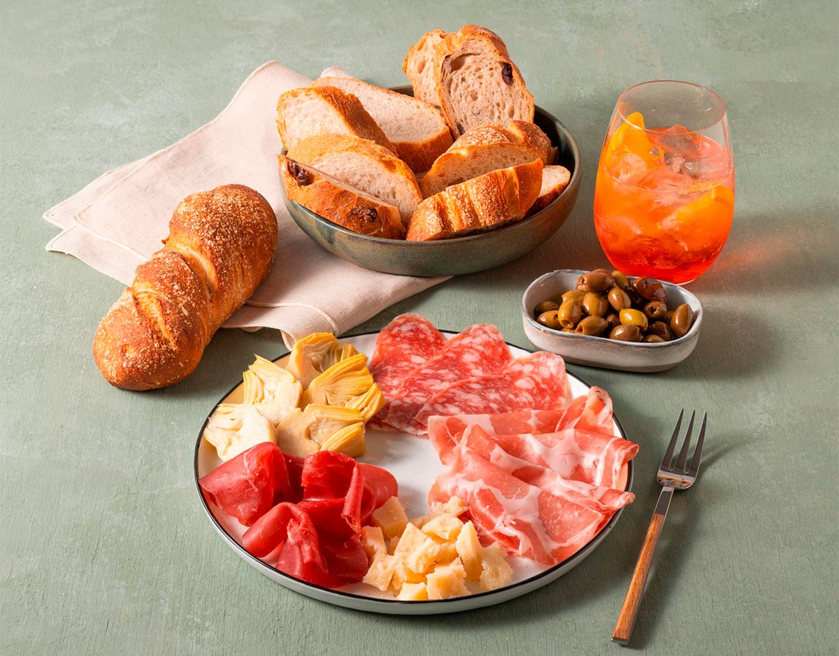 Baguette mit Antipasti-Platte, Oliven und einem orangefarbenen Getränk.