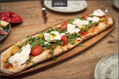 Pizza Burrata auf einem Holzbrett am Tisch.